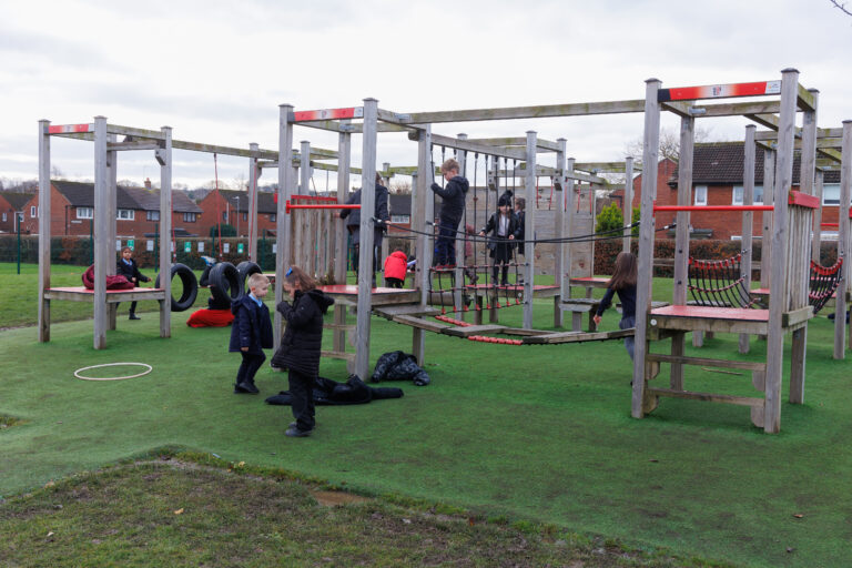 A group of children playing outside in a park in an obstacle course made of wood.