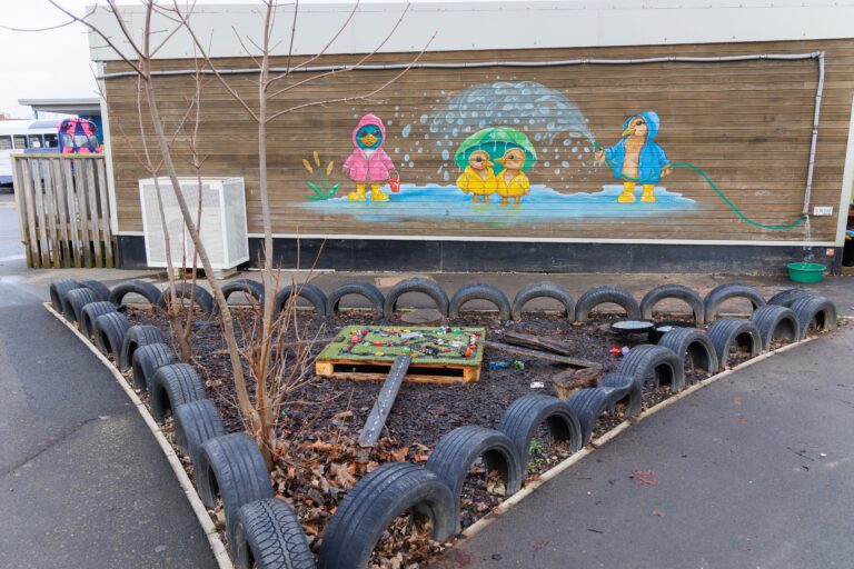 A picture of a playground with a painted wall in the background, and bark on the ground, bordered by tires.