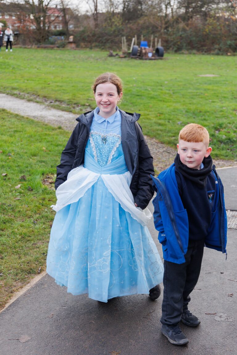 A girl and a boy standing next to each other in a playground. The boy is wearing a blue jacket and black uniform, while the girl is wearing a baby blue dress.