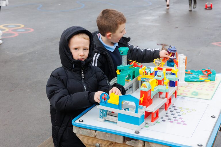 Two kids playing with toys outside. They are wearing black jackets.