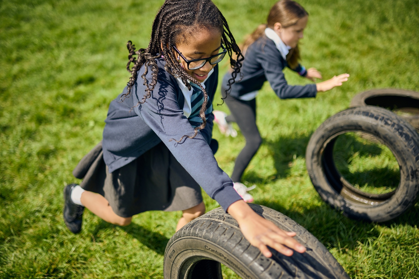 Two girls rolling tyres in a school field.
