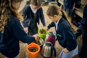 A photo of three children playing in a mud kitchen at school.